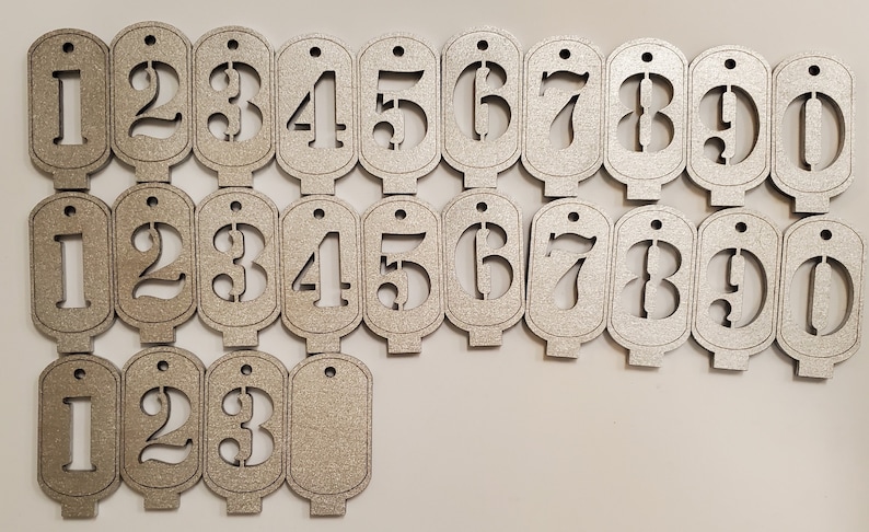 May include: Set of twenty silver-coloured wooden tags with numbers 1 through 10, each number appearing twice. The tags are shaped like a rectangle with rounded corners and have a hole at the top for hanging.