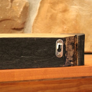 May include: A dark wood shelf with a metal hanging bracket on the back. The shelf is made from reclaimed wood and has a rustic look.