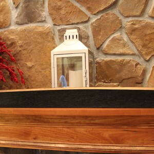 May include: A black wooden shelf made from a reclaimed wine barrel with metal brackets for hanging on a wall. The shelf is mounted on a wooden mantel above a stone fireplace.