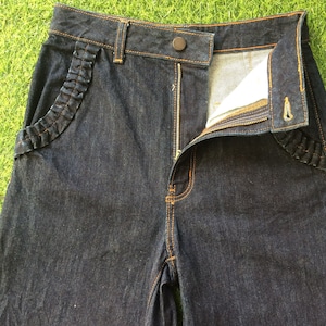 May include: Dark blue denim jeans with a zipper fly and a ruffled detail on the front pockets.
