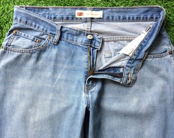 May include: Light blue denim jeans with a button and zipper closure. The jeans have a classic five-pocket design and a faded wash. The Levi's brand label is visible on the waistband.
