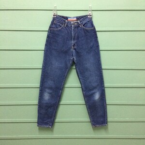 Puede incluir: Un par de pantalones vaqueros azules de mezclilla con cintura alta y pierna recta. Los vaqueros tienen un aspecto descolorido y están colgados de una percha.
