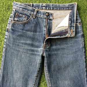 Puede incluir: Un par de pantalones vaqueros azules de mezclilla con cierre de cremallera y botón. Los vaqueros tienen un estilo clásico de cinco bolsillos y están hechos de una tela suave y cómoda.