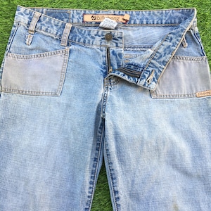 Puede incluir: Vaqueros de mezclilla azul claro con cierre de cremallera y dos bolsillos grandes de parche en la parte delantera. Los vaqueros tienen un logotipo de Billabong en el bolsillo trasero y la cintura.