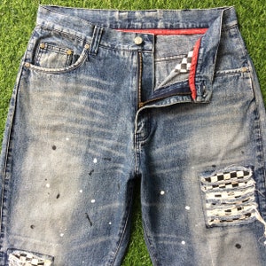 May include: Distressed blue denim jeans with white paint splatters and a checkered patch on the right leg.