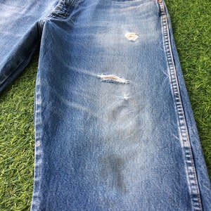 May include: A pair of blue denim jeans with distressed details, including a small hole on the right knee and a larger hole on the left knee. The jeans have a faded look and are made of a soft, comfortable fabric.