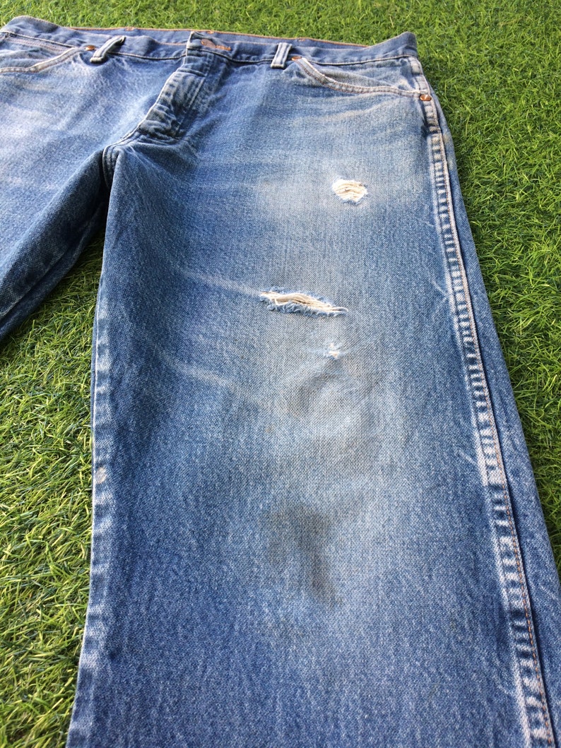 May include: A pair of blue denim jeans with distressed details, including a small hole on the right knee and a larger hole on the left knee. The jeans have a faded look and are made of a soft, comfortable fabric.