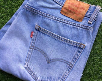 May include: Light blue denim jeans with a back pocket and a red Levi's label. The jeans have a brown leather patch with the Levi's logo and the text "501®" and "36 30".