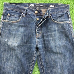 May include: Dark blue denim jeans with a button fly and classic five-pocket design. The jeans have a straight leg fit and a faded wash. The brand "Lee" is visible on the waistband. The waist size is 32 inches.