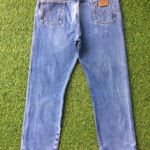 May include: A pair of blue denim jeans with a brown leather patch on the back pocket that says "Wrangler".