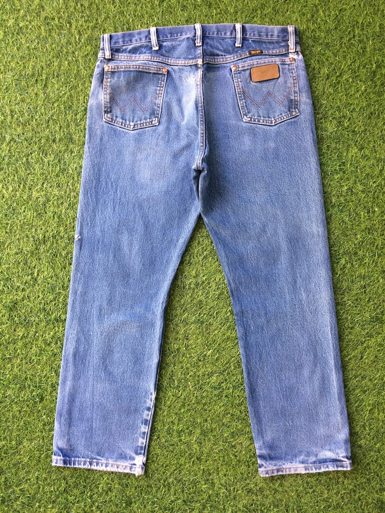 May include: A pair of blue denim jeans with a brown leather patch on the back pocket that says "Wrangler".