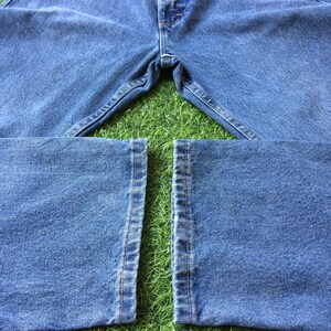May include: A pair of blue denim jeans laid out on a green grassy surface. The jeans are folded in half, with the legs of the jeans laying flat on the grass.
