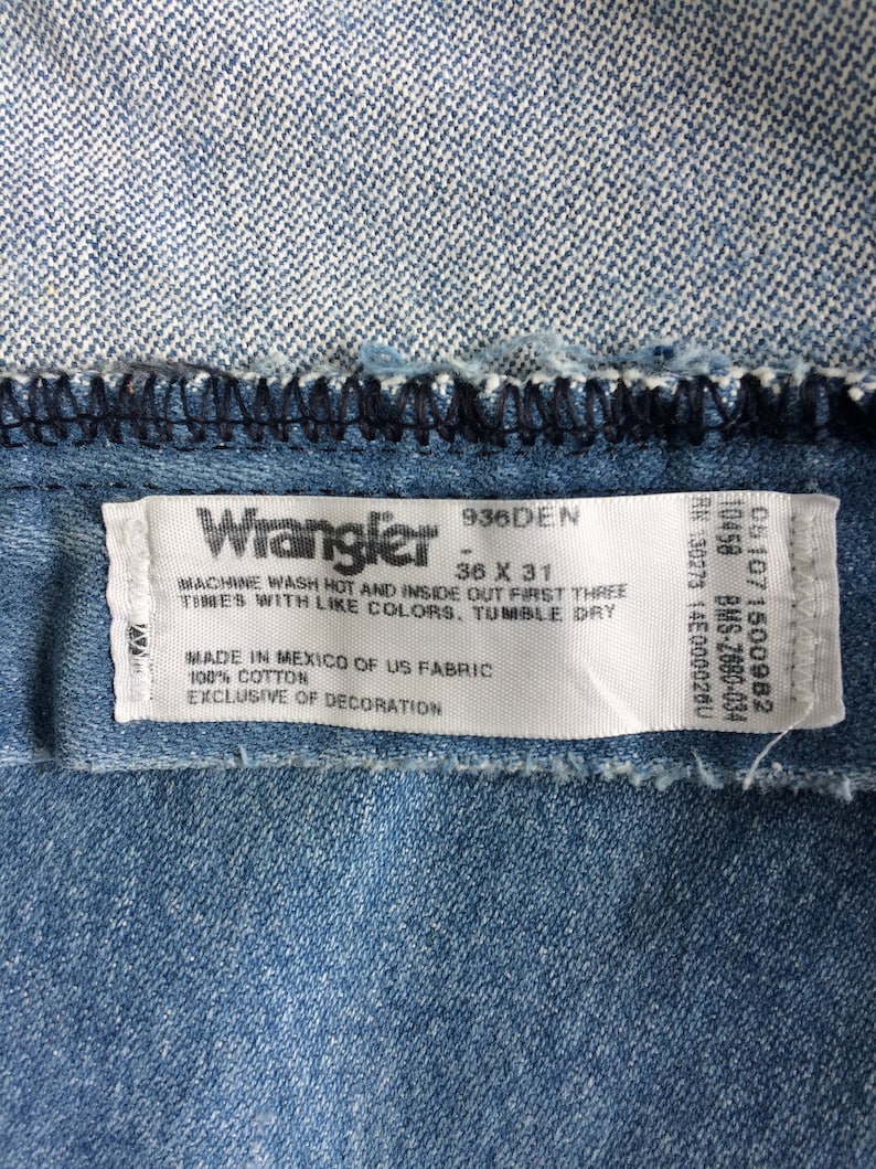 May include: A blue denim label with white text that reads "Wrangler 936DEN 36 X 31" and "MACHINE WASH HOT AND INSIDE OUT FIRST THREE TIMES WITH LIKE COLORS, TUMBLE DRY MADE IN MEXICO OF US FABRIC 100% COTTON EXCLUSIVE OF DECORATION".