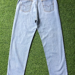 May include: A pair of light blue denim jeans with a brown leather patch on the back waistband. The jeans have a classic five-pocket style and a straight leg.