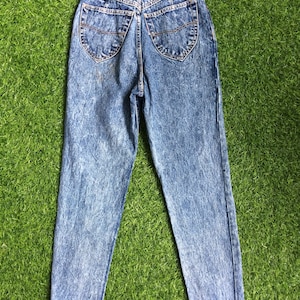 May include: A pair of blue acid wash denim jeans with a brown leather patch on the back that says "Something" and "Low Rise".
