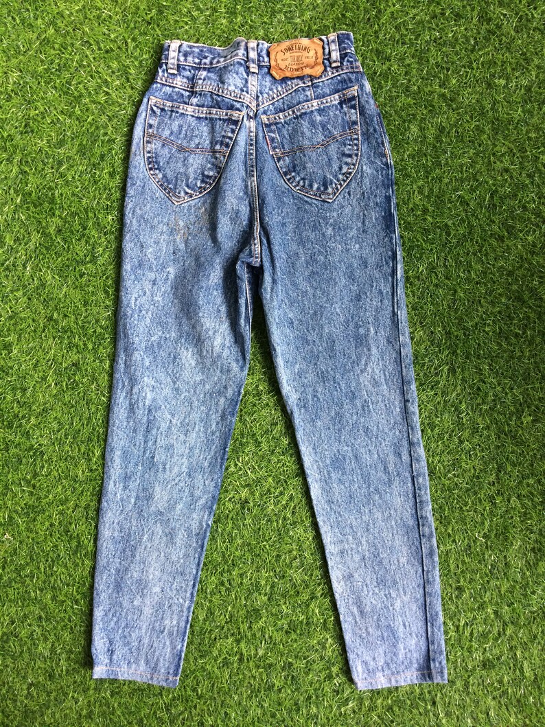 May include: A pair of blue acid wash denim jeans with a brown leather patch on the back that says "Something" and "Low Rise".