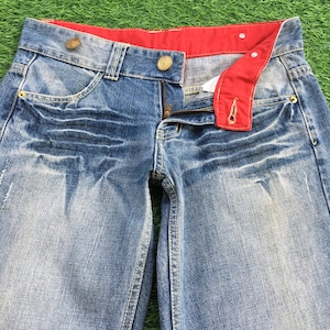 Könnte beinhalten: Hellblaue Jeans mit rotem Bund und Knopfdetails. Die Jeans haben eine verwaschene Optik und einen Reißverschluss. Das Design umfasst Vordertaschen und einen klassischen Fünf-Taschen-Stil.