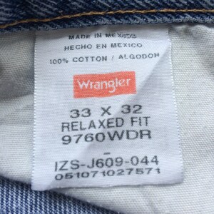 Pode incluir: Uma etiqueta branca com texto preto e um logotipo vermelho Wrangler. A etiqueta diz "Made in Mexico", "Hecho en Mexico", "100% Cotton / Algodon", "33 x 32", "Relaxed Fit", "9760WDR", "IZS-J609-044" e "051071027571".