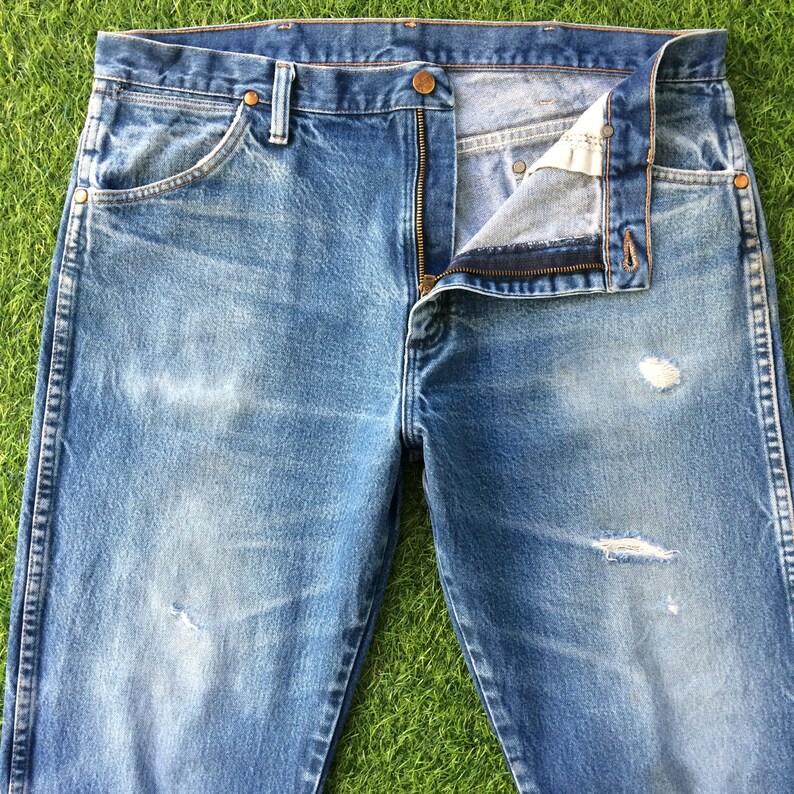 May include: A pair of light blue denim jeans with a zip fly and a distressed look. The jeans have a faded appearance and several small holes.