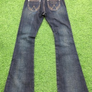 May include: Dark wash denim jeans with a flared leg design. The jeans feature classic five-pocket styling, with decorative stitching on the back pockets and the brand name "WRA" on the waistband.