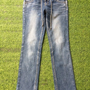 May include: Light blue denim jeans with a drawstring waist and a classic five-pocket design. The jeans have a faded wash and a slight bootcut leg opening. The waistband is black with a red accent.