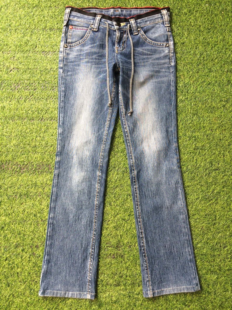 May include: Light blue denim jeans with a drawstring waist and a classic five-pocket design. The jeans have a faded wash and a slight bootcut leg opening. The waistband is black with a red accent.