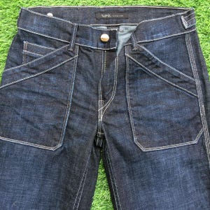Może przedstawiać: Jeans z ciemnoniebieskiego denimu z białymi szwami. Jeans mają prosty krój i luźny fason. Jeans mają metkę z logo "Nudie" i "Selvedge Denim".