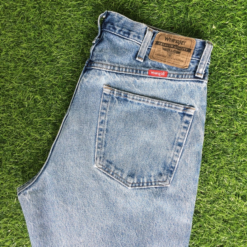 May include: A pair of light blue denim jeans with a back pocket and a brown leather Wrangler label with the text "Wrangler Premium Quality" and "Comfort Guaranteed".