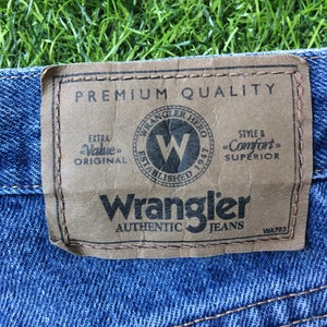 May include: A brown leather patch with the text "Premium Quality" and "Wrangler Authentic Jeans" in black. The patch also features a logo with the text "Wrangler Hero Established 1947" and a large "W" inside a circle.