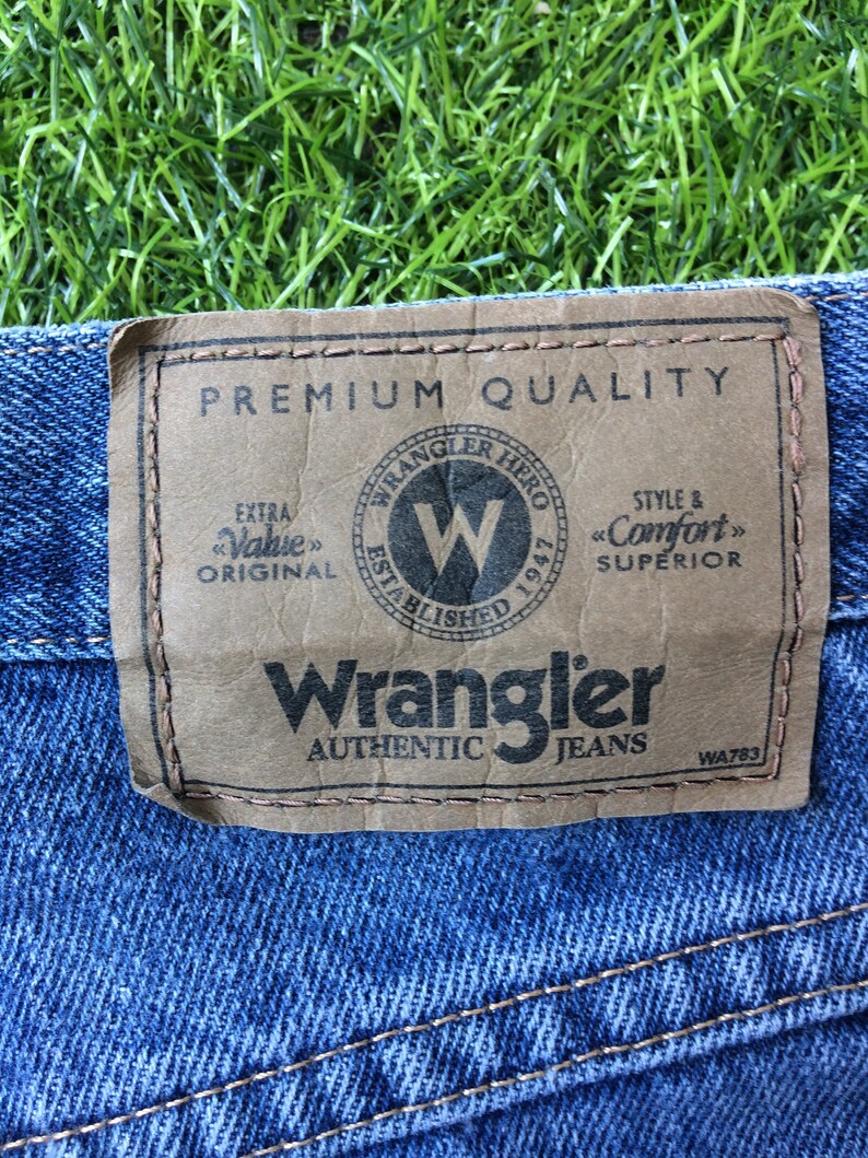 May include: A brown leather patch with the text "Premium Quality" and "Wrangler Authentic Jeans" in black. The patch also features a logo with the text "Wrangler Hero Established 1947" and a large "W" inside a circle.