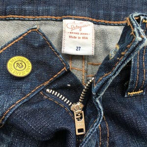 May include: A white ceramic mug with a black handle and the text "But First, Coffee" in a black, handwritten-style font. The mug is on a white surface.