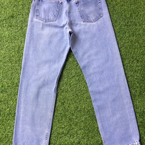 Pode incluir: Um par de cal&ccedil;as de ganga azul claro com um remendo de couro castanho no bolso de tr&aacute;s que diz "Wrangler Westernwear".
