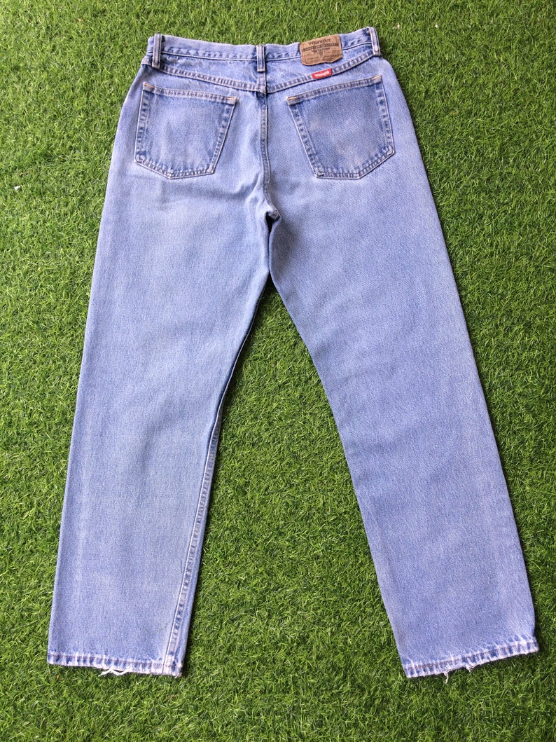 Pode incluir: Um par de cal&ccedil;as de ganga azul claro com um remendo de couro castanho no bolso de tr&aacute;s que diz "Wrangler Westernwear".