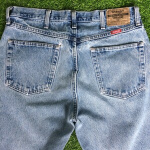 May include: A pair of light blue denim jeans with a back pocket on each side. The jeans have a brown leather patch with the text "Wrangler Premium Quality" and a small red tag with the text "Wrangler" on the right back pocket.