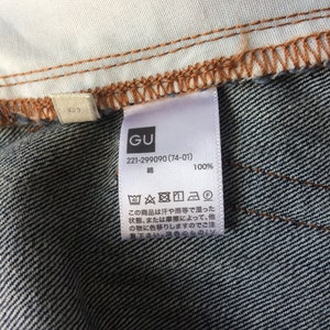 以下が含まれることがあります： 「GU 221-299090 (74-01) 綿 100%」と黒文字で書かれた白いタグ。タグには洗濯表示のシンボルも付いている。