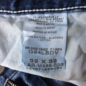 May include: A blue denim jean label with white stitching. The label has white text on a blue background with the text "VF Jeanswear LP 1481 South Elm Street Greensboro, NC 27406 Made in Mexico Hecho en Mexico Fabrique au Mexique 100% Cotton/Algodon/Coton 6K000194D 71253 G94LSDV 32 X 32 LAR-M568-003".