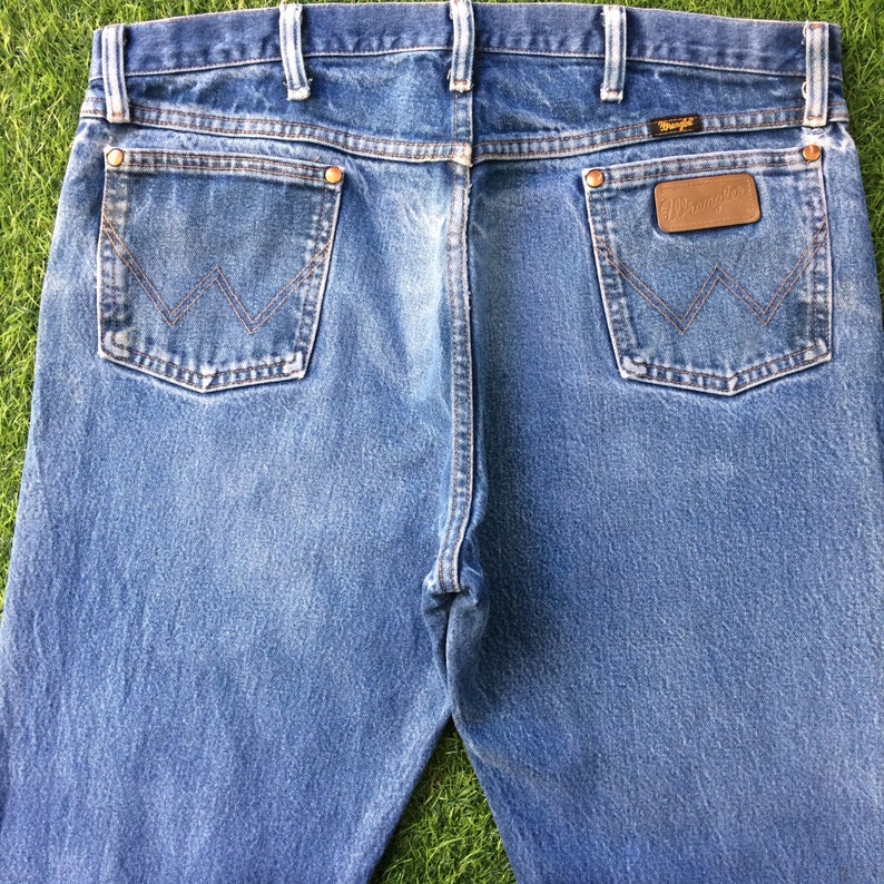 May include: A pair of blue denim jeans with a brown leather patch on the back pocket that says "Wrangler".