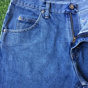 May include: A pair of blue denim jeans with a zip fly and a button fastening. The jeans have a classic five-pocket style with a front pocket on the right side and two back pockets.