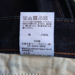 Peut inclure: &Eacute;tiquette d'entretien blanche avec des instructions de lavage et du texte japonais. L'&eacute;tiquette est fix&eacute;e &agrave; un jean bleu fonc&eacute;.