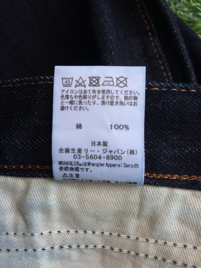 Peut inclure: &Eacute;tiquette d'entretien blanche avec des instructions de lavage et du texte japonais. L'&eacute;tiquette est fix&eacute;e &agrave; un jean bleu fonc&eacute;.