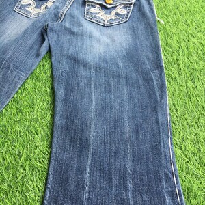 Op de afbeelding: Een paar blauwe denim jeans met witte stiksels en borduurwerk op de achterzakken. De jeans heeft een bootcut-stijl en is in goede staat.