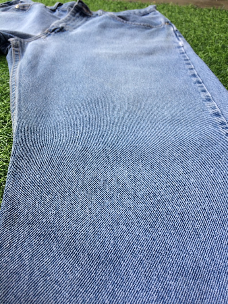 Pode incluir: Um close-up de um par de cal&ccedil;as de ganga azul claro. O tecido tem um padr&atilde;o de trama diagonal.