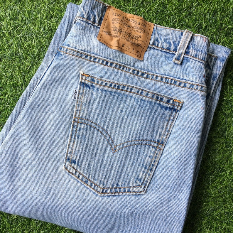 May include: Light blue denim jeans with a brown leather Levi Strauss & Co. patch and a back pocket with a brown stitching detail. The patch has the text "Levi Strauss & Co.", "ORIGINAL  Rivetted  Quality  Clothing", and "W 38 L 32".