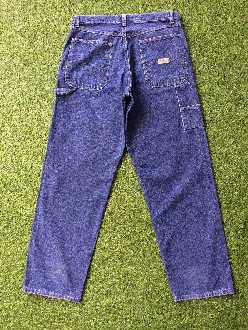 May include: A pair of blue denim carpenter jeans with a brand label on the back right pocket.