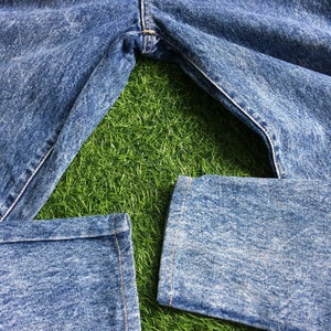 May include: A pair of blue denim jeans with a faded wash, laid out on a green grassy surface. The jeans have a straight leg and are cuffed at the bottom.