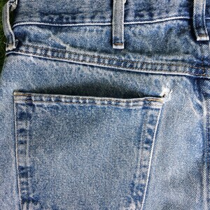 May include: A close-up of the back pocket of a pair of blue denim jeans. The pocket has a light blue denim fabric and is stitched with brown thread.