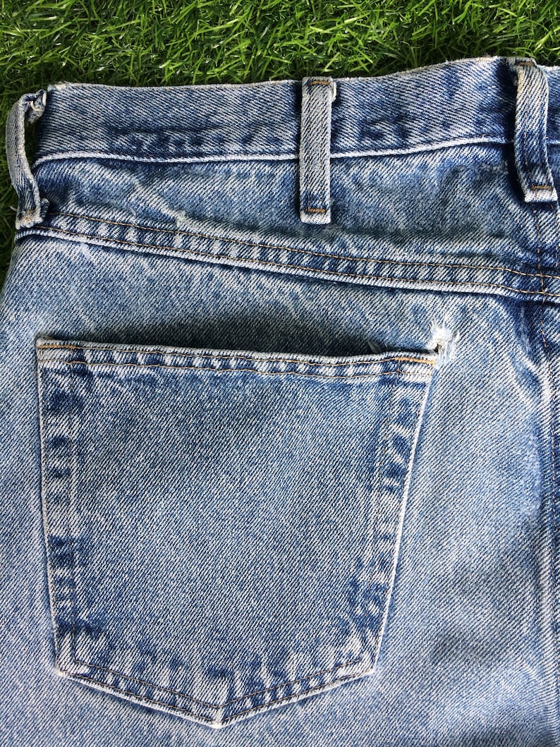 May include: A close-up of the back pocket of a pair of blue denim jeans. The pocket has a light blue denim fabric and is stitched with brown thread.