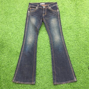 May include: Dark wash denim jeans with a flared leg design. The jeans feature a classic five-pocket style, a button and zipper closure, and contrasting stitching. The denim has a faded, worn look, with subtle distressing.
