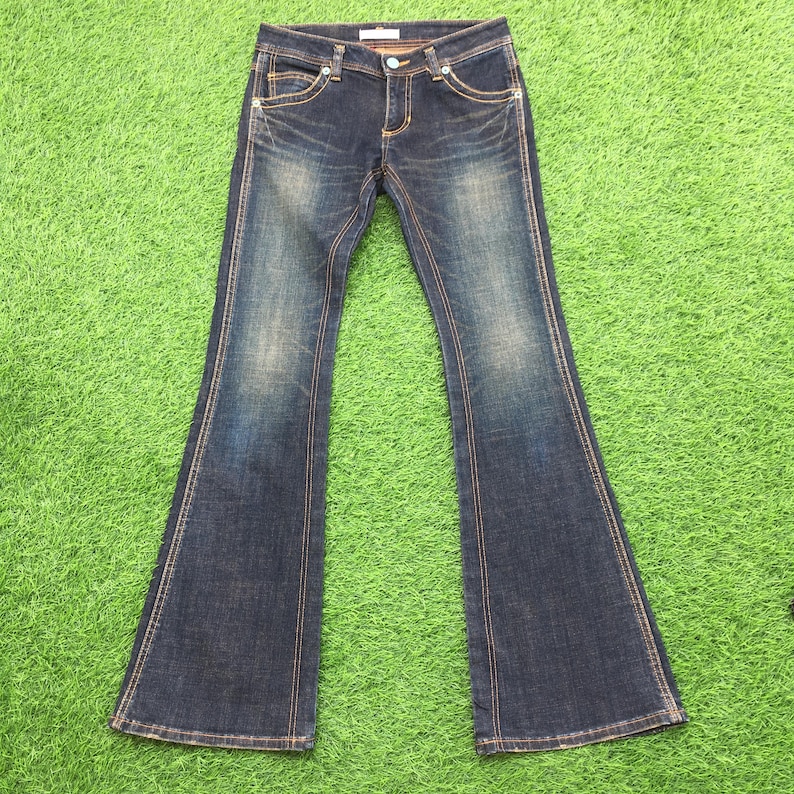 May include: Dark wash denim jeans with a flared leg design. The jeans feature a classic five-pocket style, a button and zipper closure, and contrasting stitching. The denim has a faded, worn look, with subtle distressing.