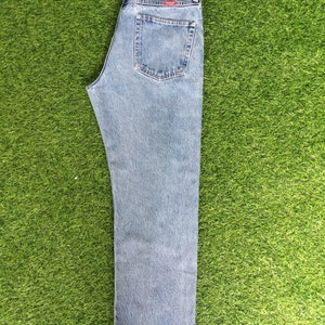 May include: A pair of light blue denim jeans with a brown leather patch on the back waistband that says "Wrangler" and "Premium Western Denim".
